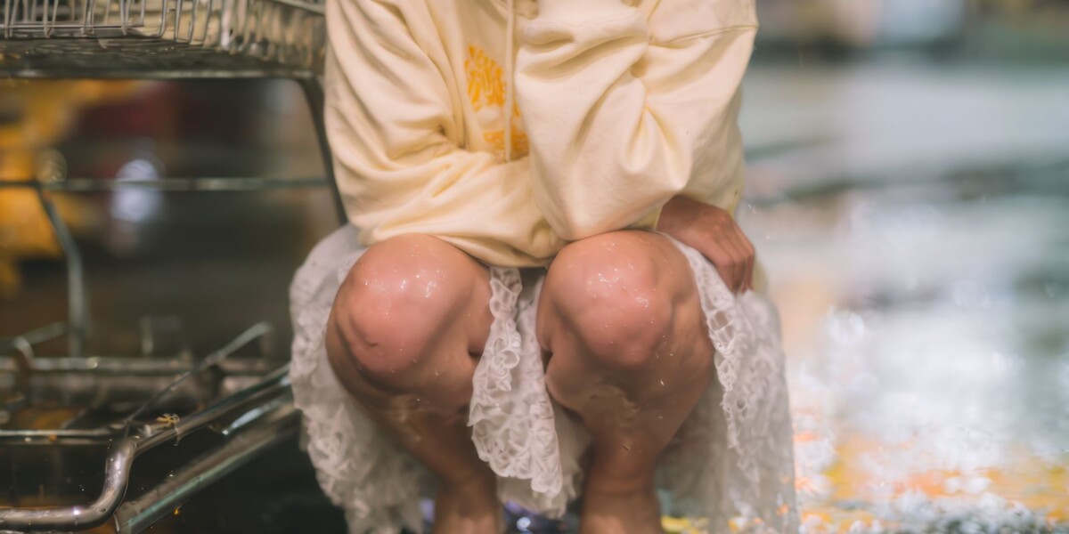 雨の日のスーパーの駐車場でしゃがむ女性